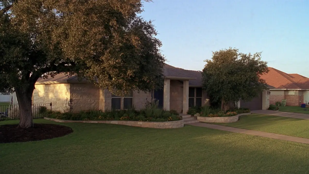 After: The same front yard with a thick green lawn and tidy beds.